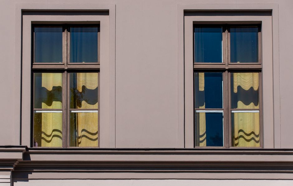 Two symmetrical windows with yellow curtains on an urban building facade.