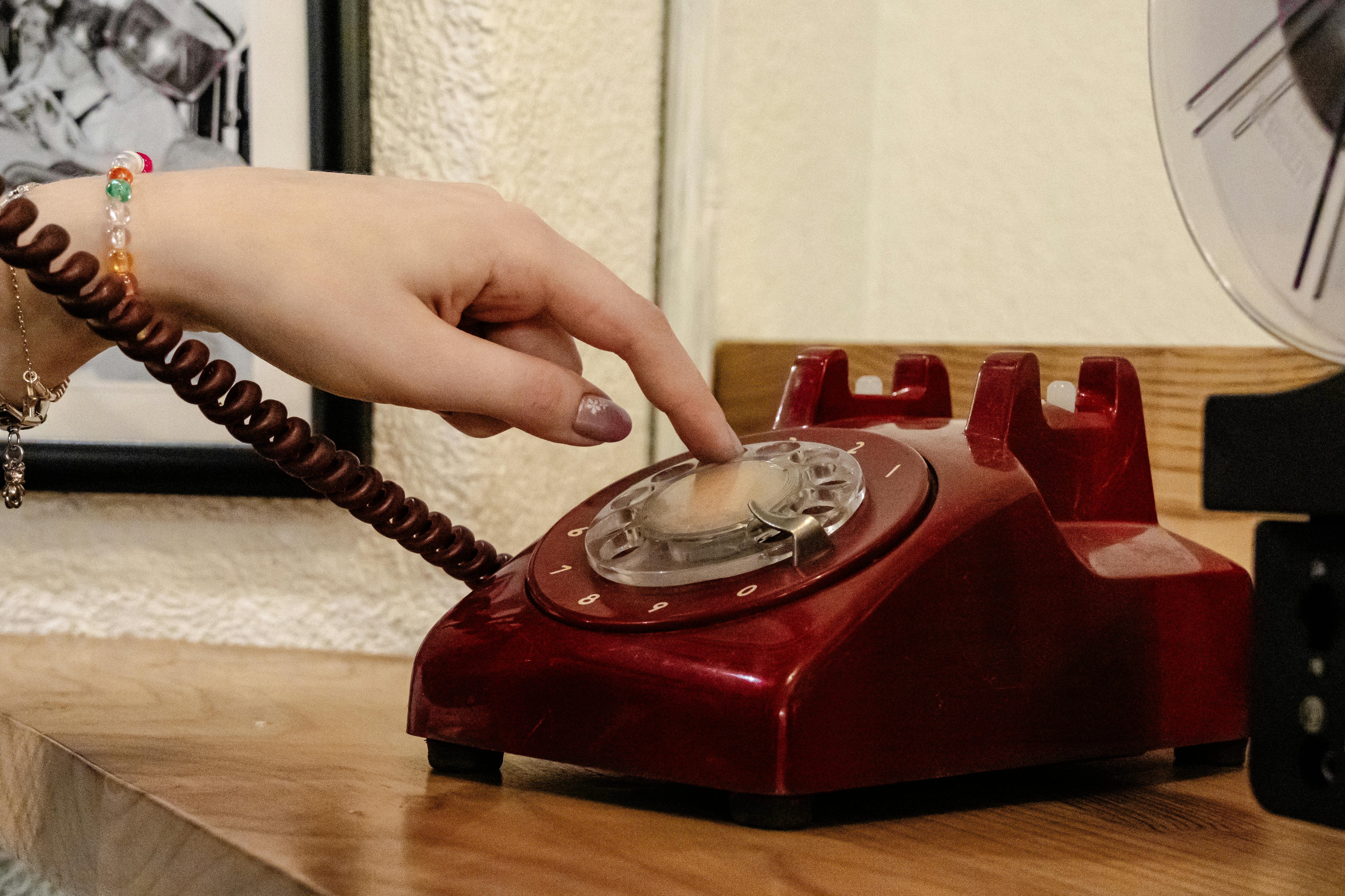 Free A close-up of a hand dialing a classic red rotary phone, capturing nostalgia. Stock Photo