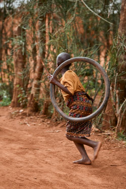 Free A joyful child runs with a hoop along a dirt path surrounded by trees in a rural area. Stock Photo