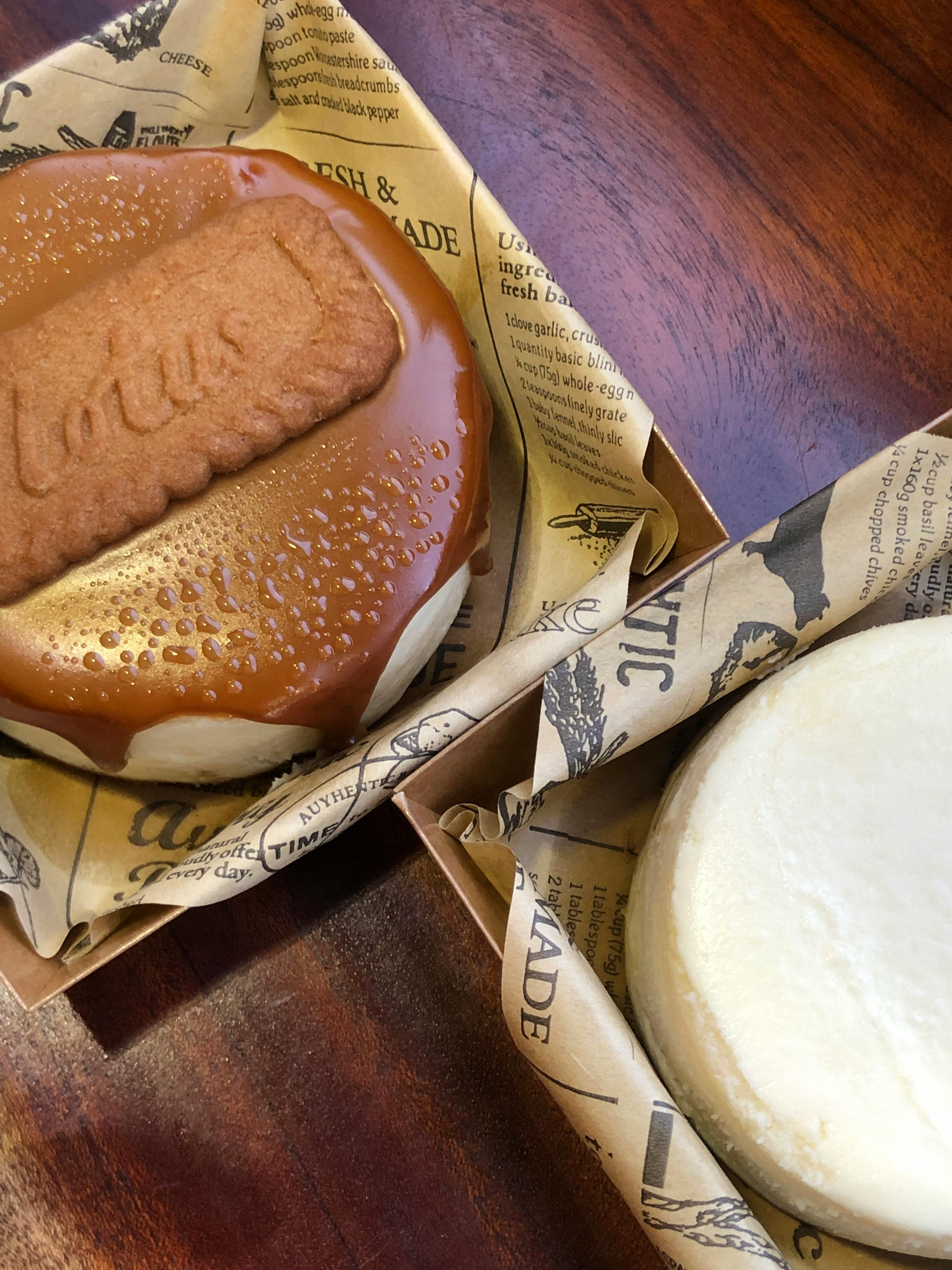 Top view of two cheesecakes, one with a caramel Lotus biscuit topping on a wooden table.