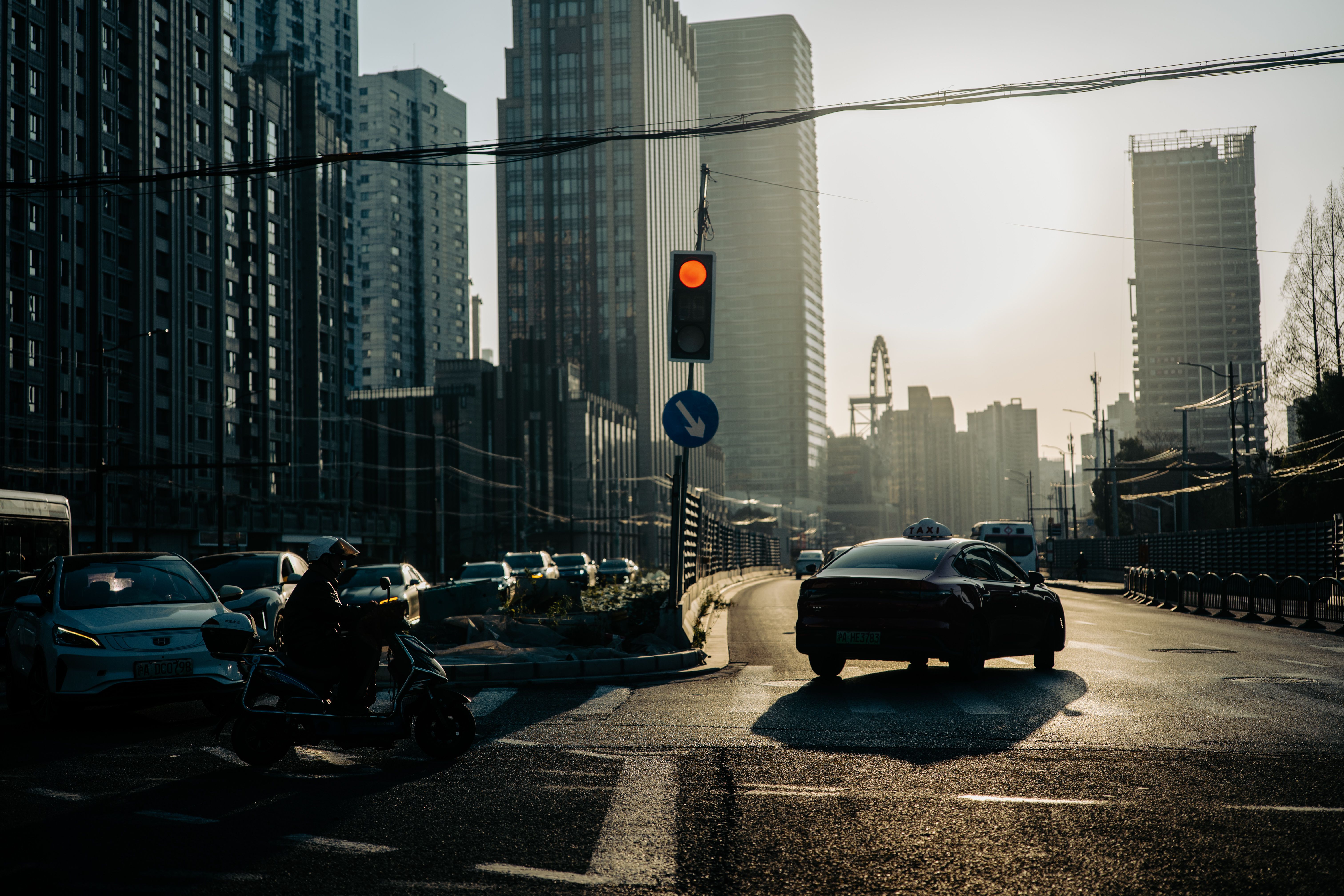 Bustling city street in Shanghai with cars and motorbikes at a red light during sunset.