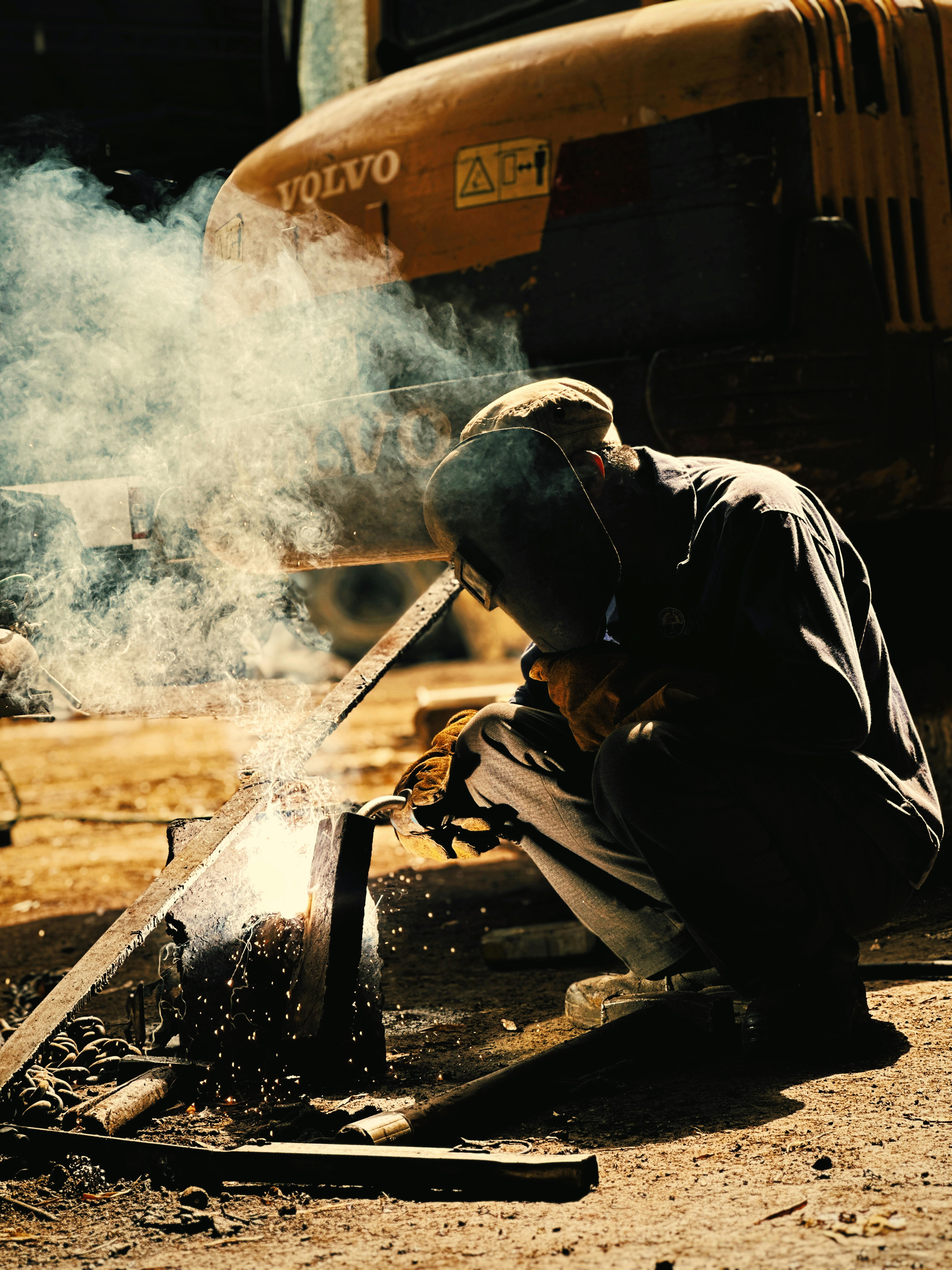 A welder performs metalwork on a construction site in Vietnam, under a bright, smoky atmosphere.