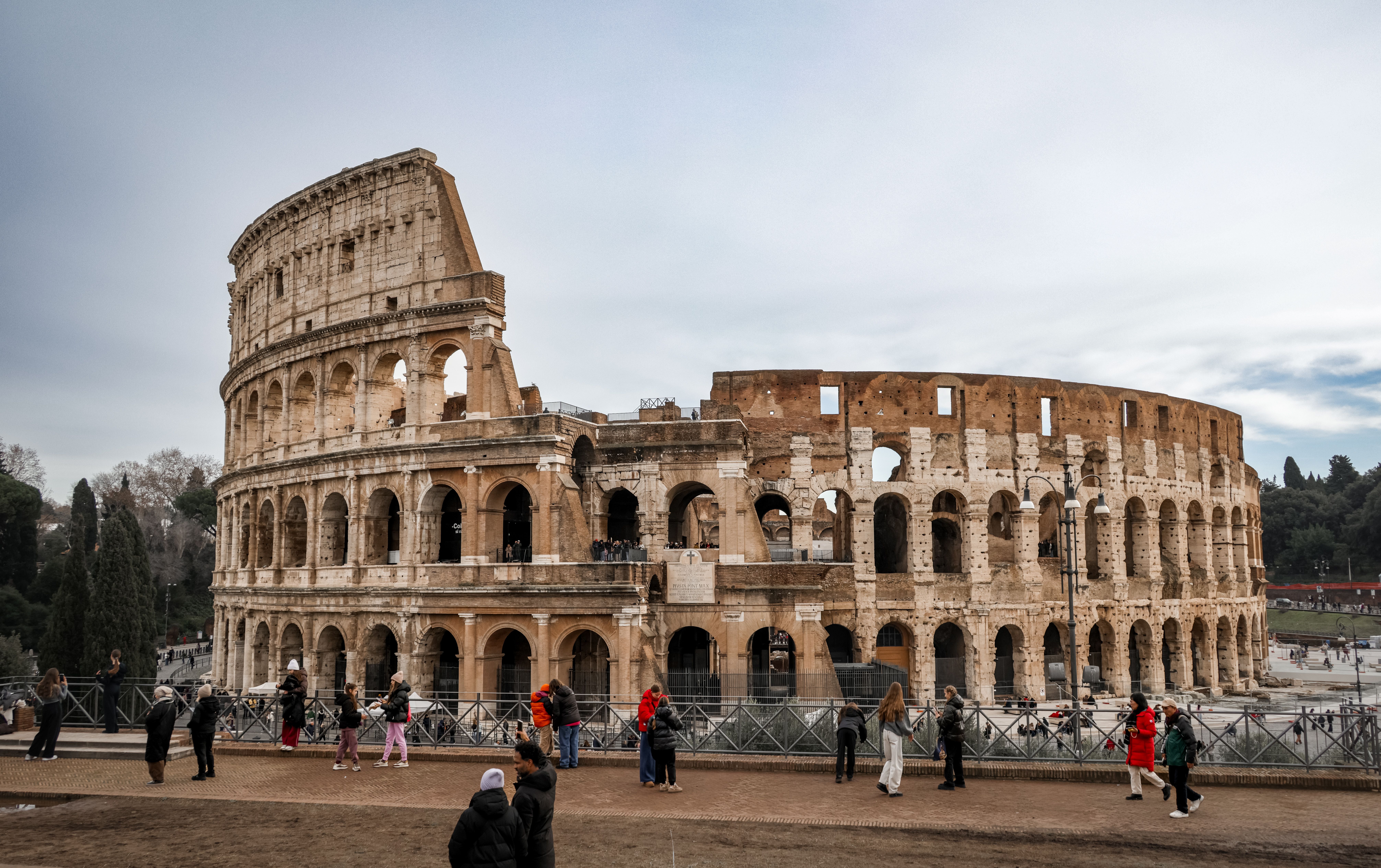 View of the ancient Colosseum in Rome with tourists exploring the historic landmark.