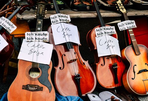 Een verzameling vintage snaarinstrumenten tentoongesteld op een openluchtmarkt, met bordjes waarop staat dat ze te koop zijn