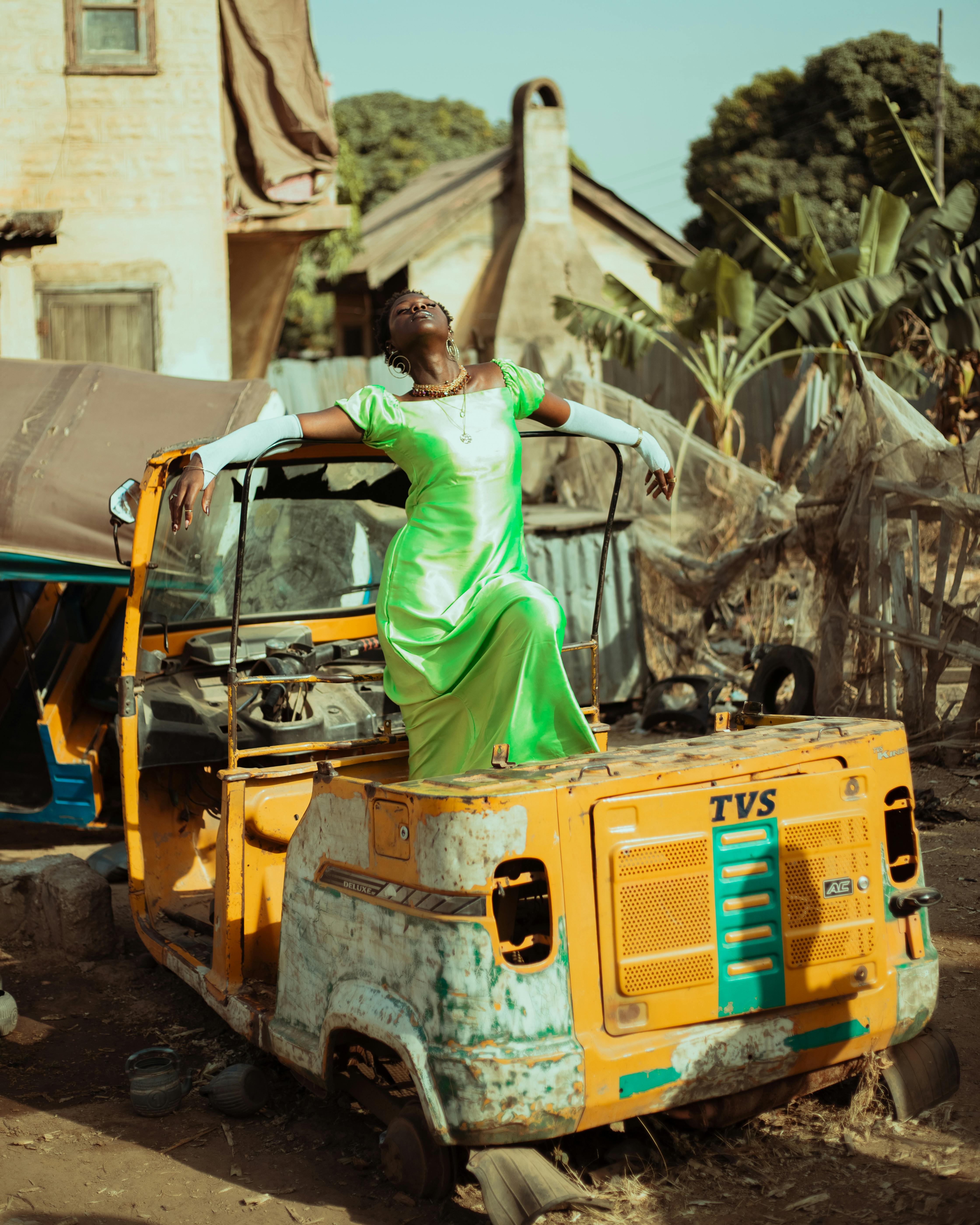 Elegant woman in green dress poses on rustic vehicle outdoors.
