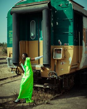 Woman in a bright green dress poses by a vintage train in an outdoor setting.
