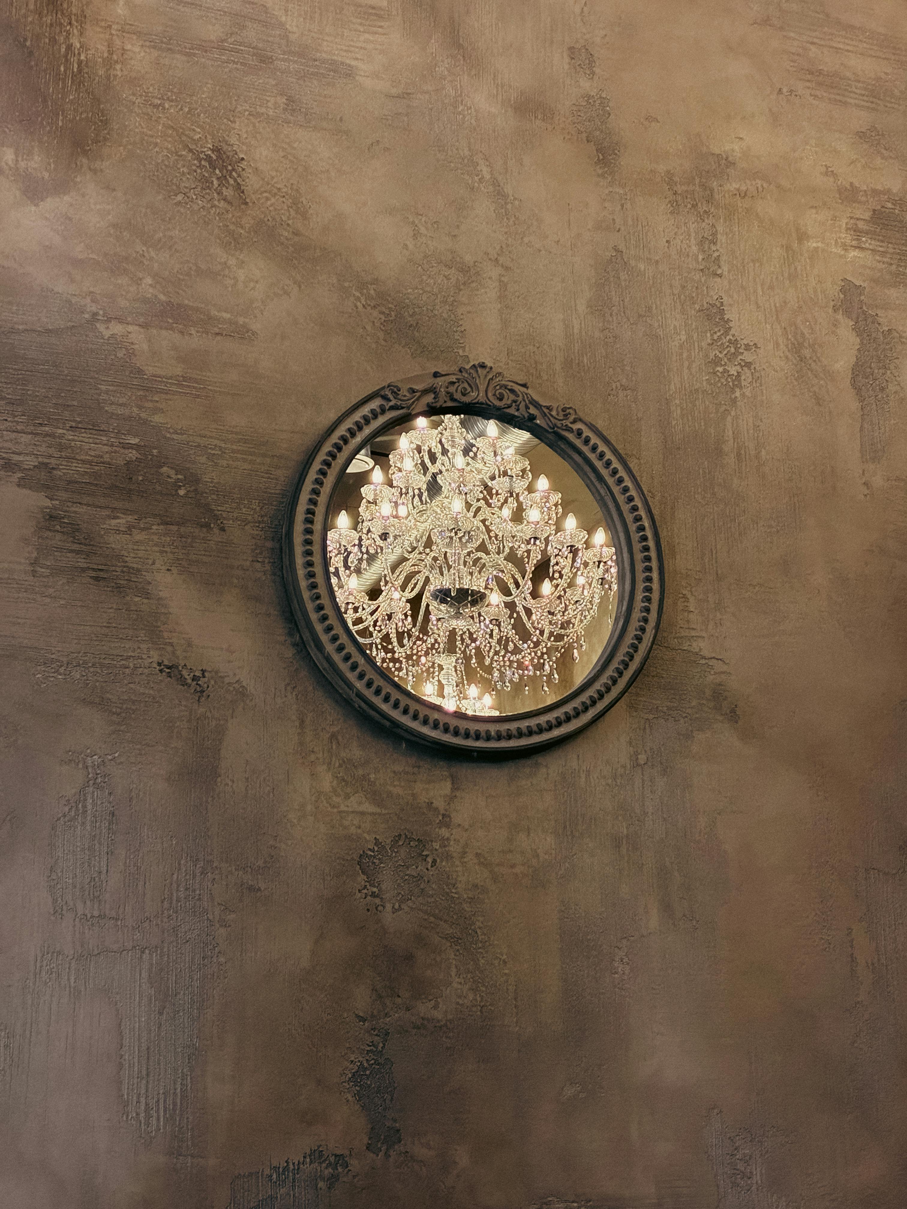 Δωρεάν Αντανάκλαση ενός κρυστάλλινου πολυελαίου σε έναν διακοσμητικό, στρογγυλό καθρέφτη σε έναν τοίχο με υφή. Φωτογραφία από στοκ φωτογραφιών