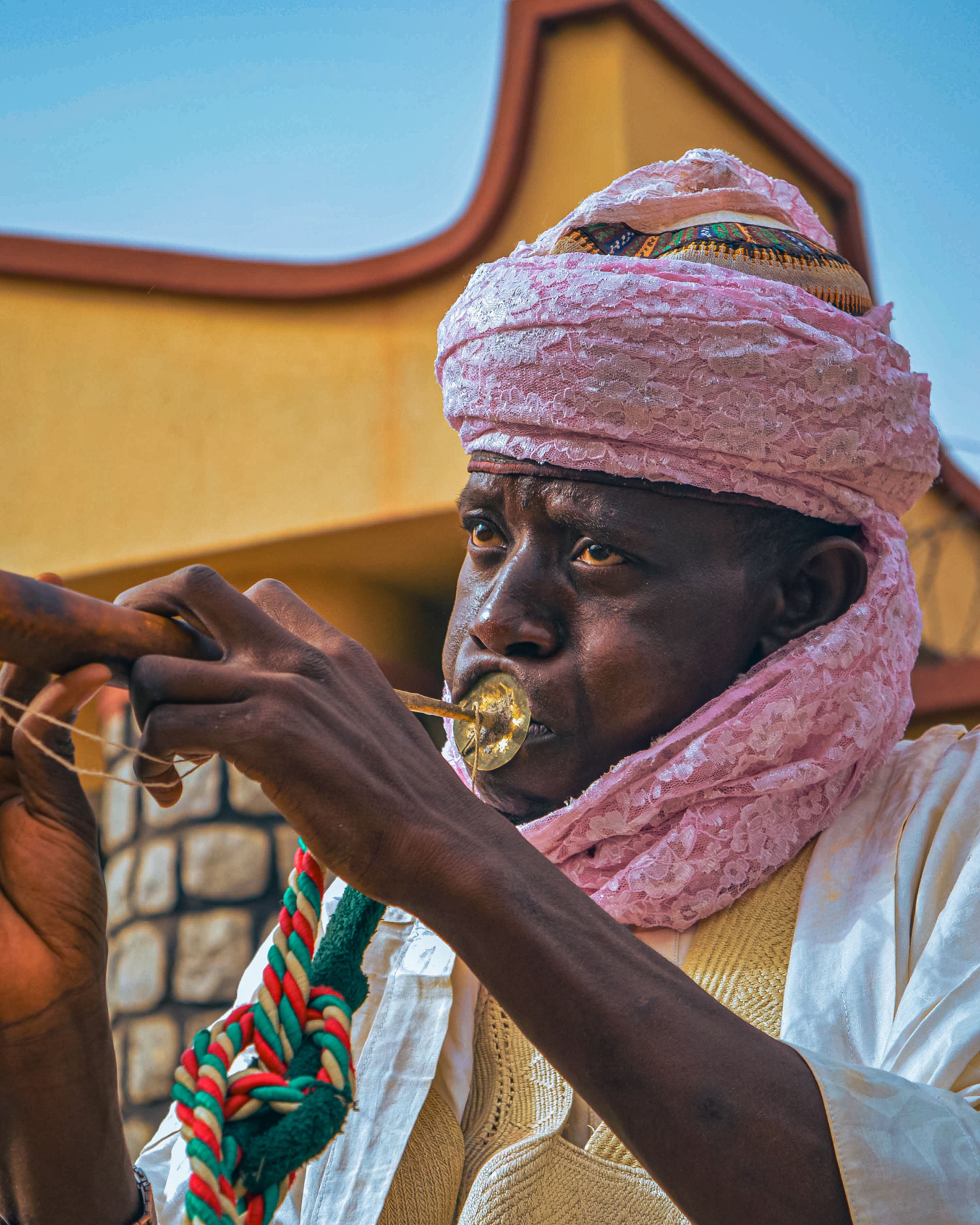 A man in traditional attire plays an African wind instrument with focus and skill.
