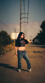 Confident young woman posing on a rural dirt road under telephone lines.