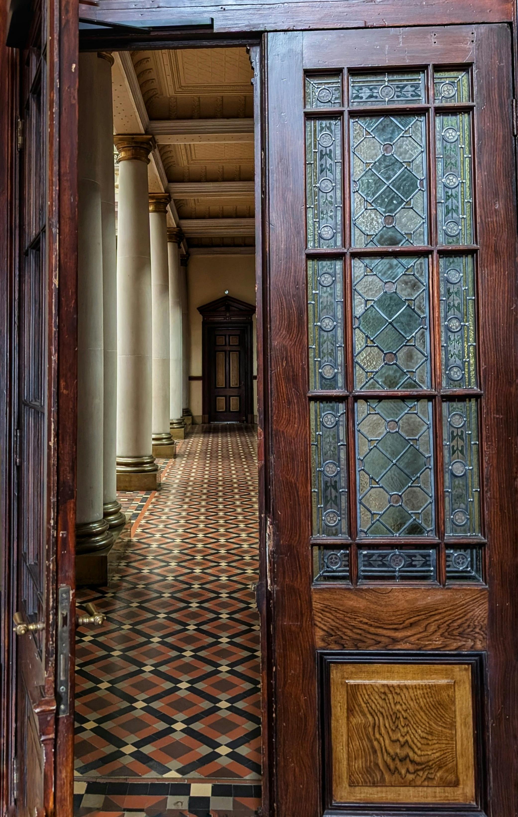 Δωρεάν Ανακαλύψτε ένα ιστορικό διάδρομο με δάπεδο με σχέδια και βιτρό πόρτα. Φωτογραφία από στοκ φωτογραφιών