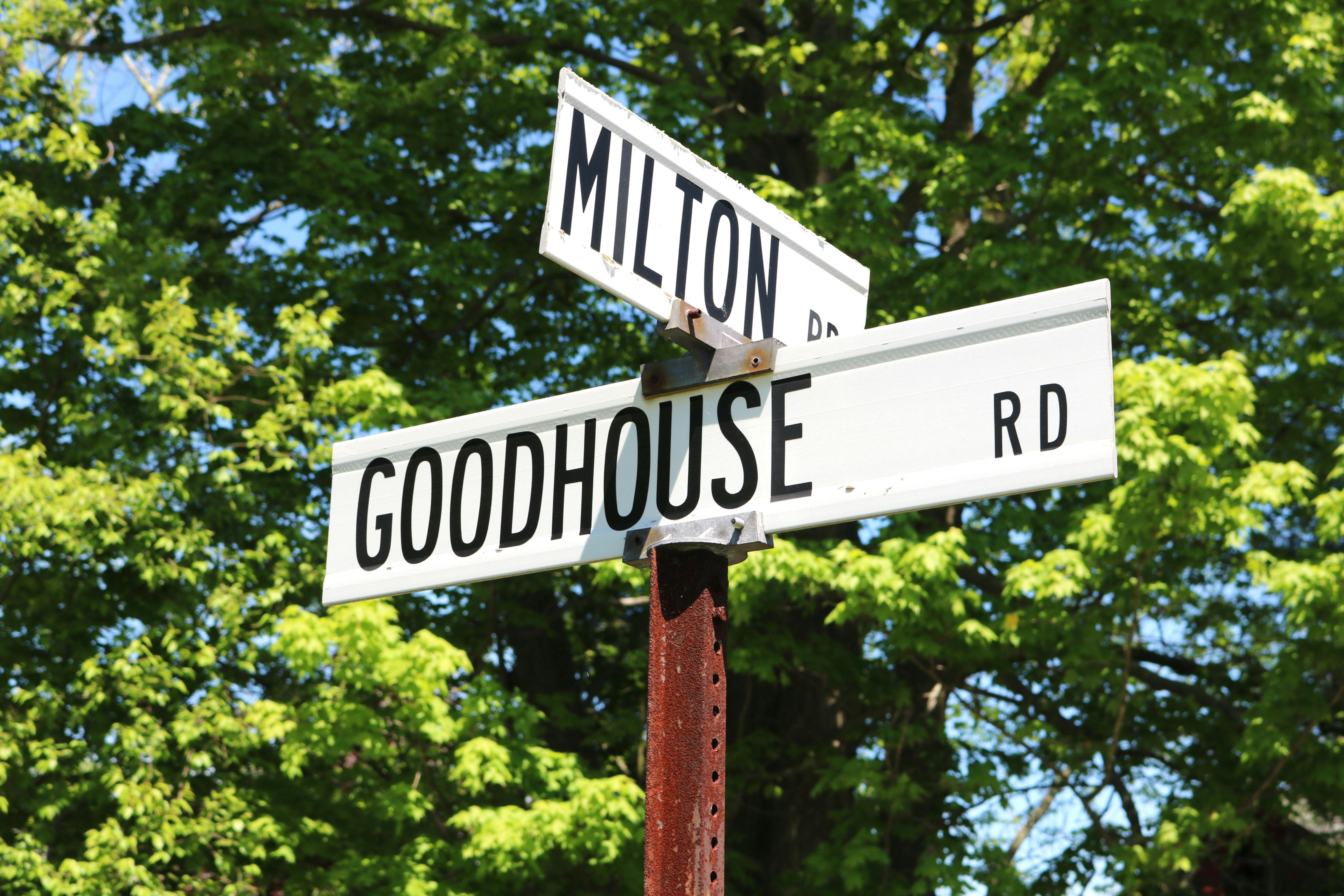 Gratis Rambu jalan untuk Milton Rd dan Goodhouse Rd dengan pepohonan di latar belakang. Foto Stok