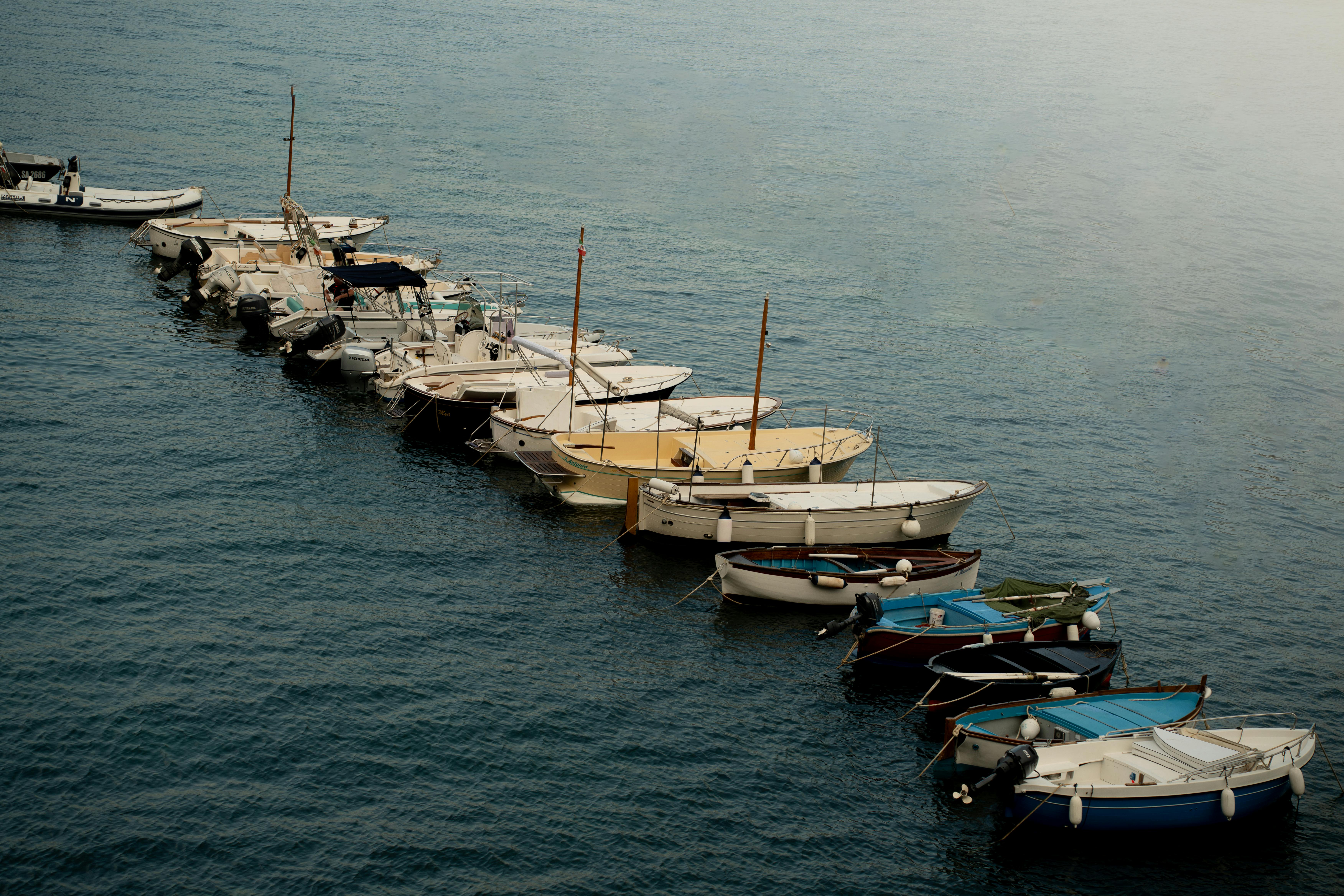 Gratis Pemandangan damai perahu-perahu kecil yang berlabuh di perairan biru yang tenang, sempurna untuk inspirasi perjalanan. Foto Stok