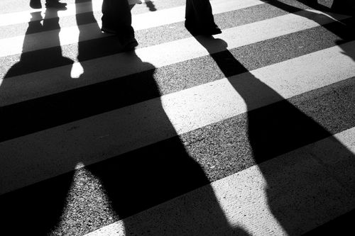 Free Silhouettes of people casting shadows while walking on a crosswalk in black and white. Stock Photo