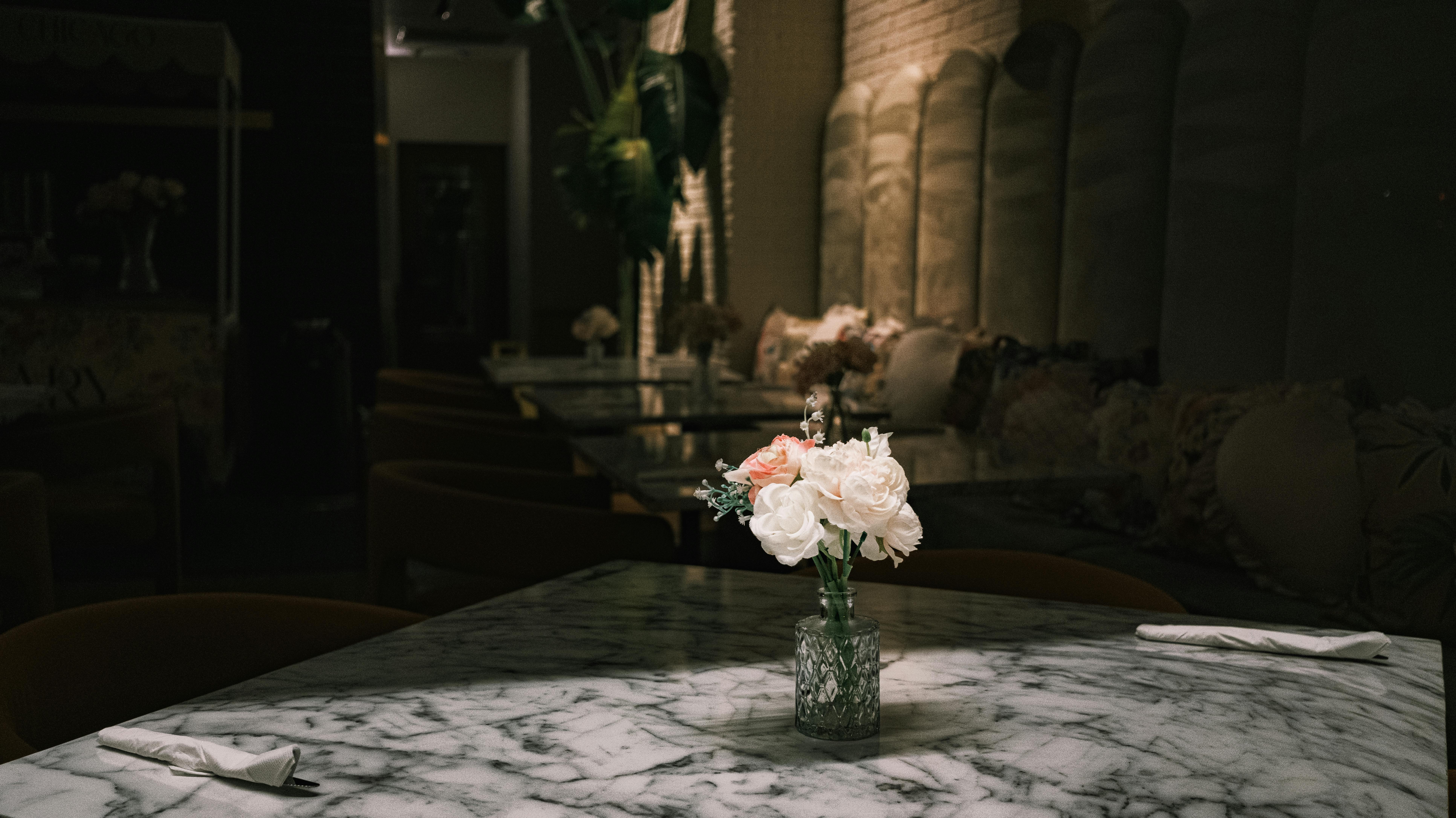 Δωρεάν Ένα όμορφα στρωμένο μαρμάρινο τραπέζι με ένα λουλουδάτο κεντρικό διακοσμητικό σε ένα αμυδρά φωτισμένο καφέ, δημιουργώντας μια ζεστή και κομψή ατμόσφαιρα. Φωτογραφία από στοκ φωτογραφιών