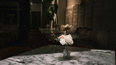 A beautifully set marble table with a floral centerpiece in a dimly lit café, creating a warm and elegant ambiance.