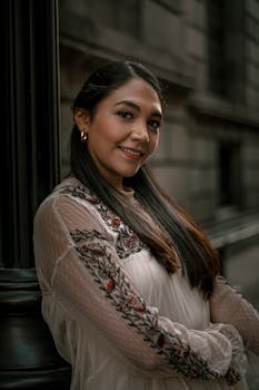 Smiling woman in an embroidered white dress posing elegantly against a textured background.
