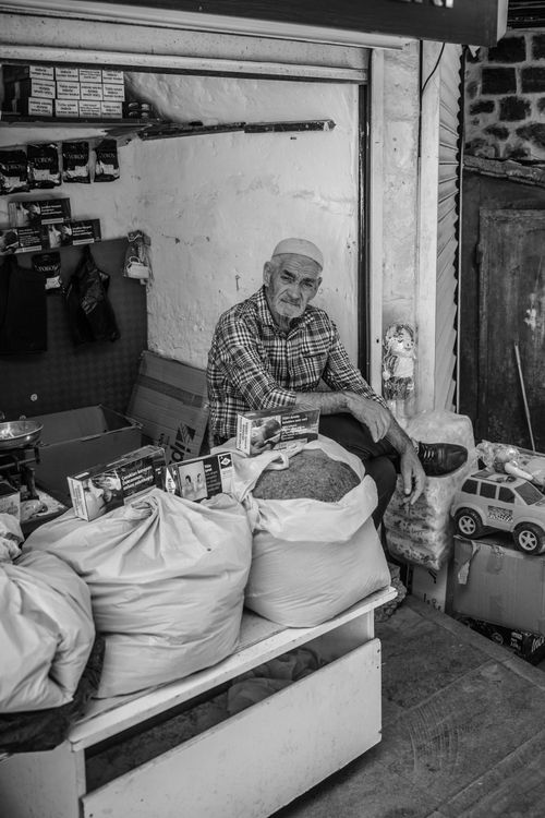 Free Black and white photo of an elderly vendor sitting with goods in a traditional market. Stock Photo