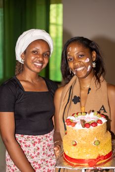 Two women celebrate a birthday holding a decorated cake with strawberries.