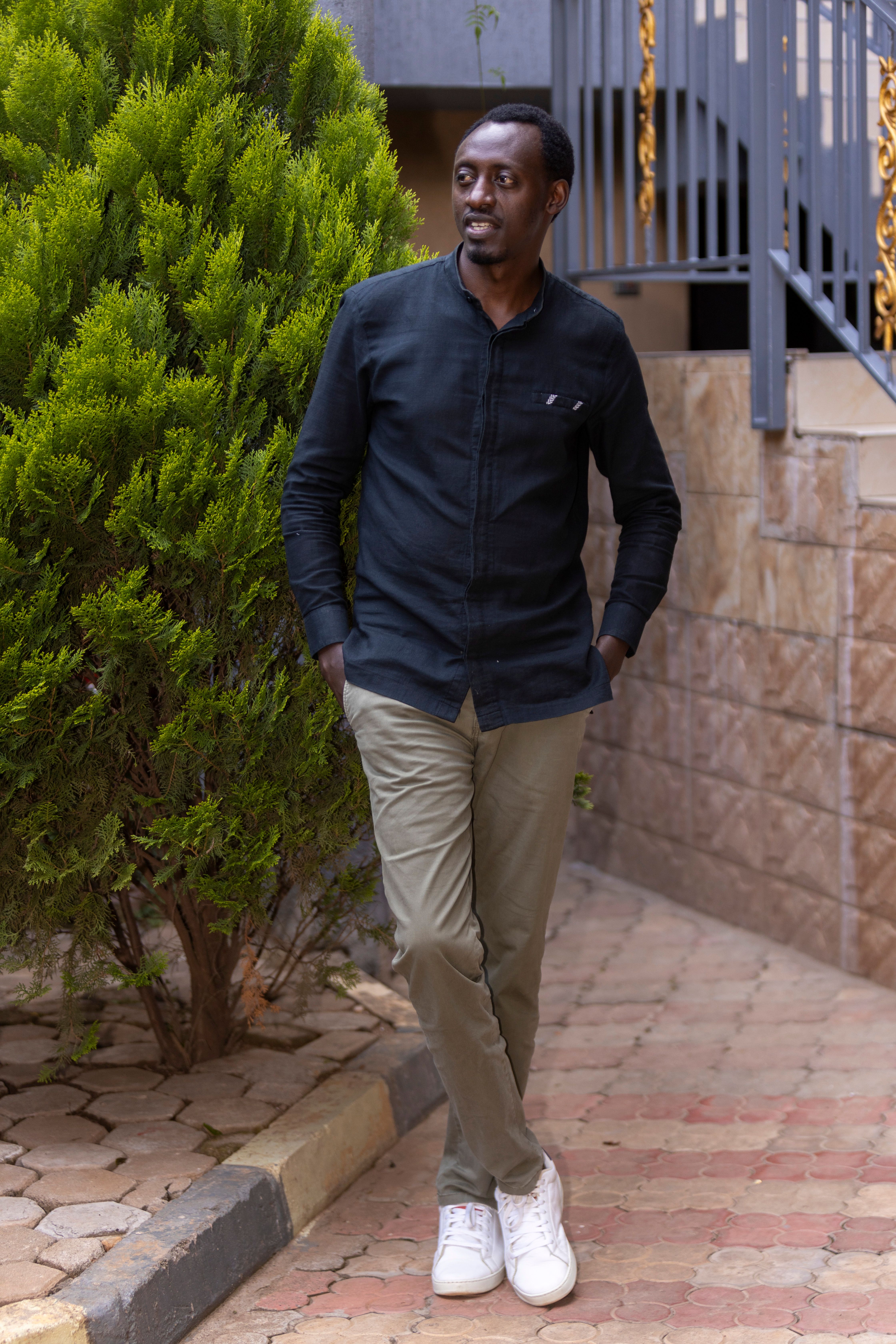 Casual fashion portrait of a man walking outdoors, leaning against a tree.