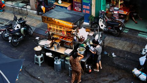 Two women preparing food at a bustling Vietnamese street food stall.