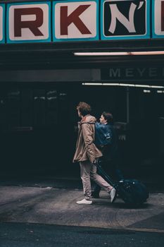 两个穿着外套的人带着行李走在城市的人行道上，透露出旅行的意味