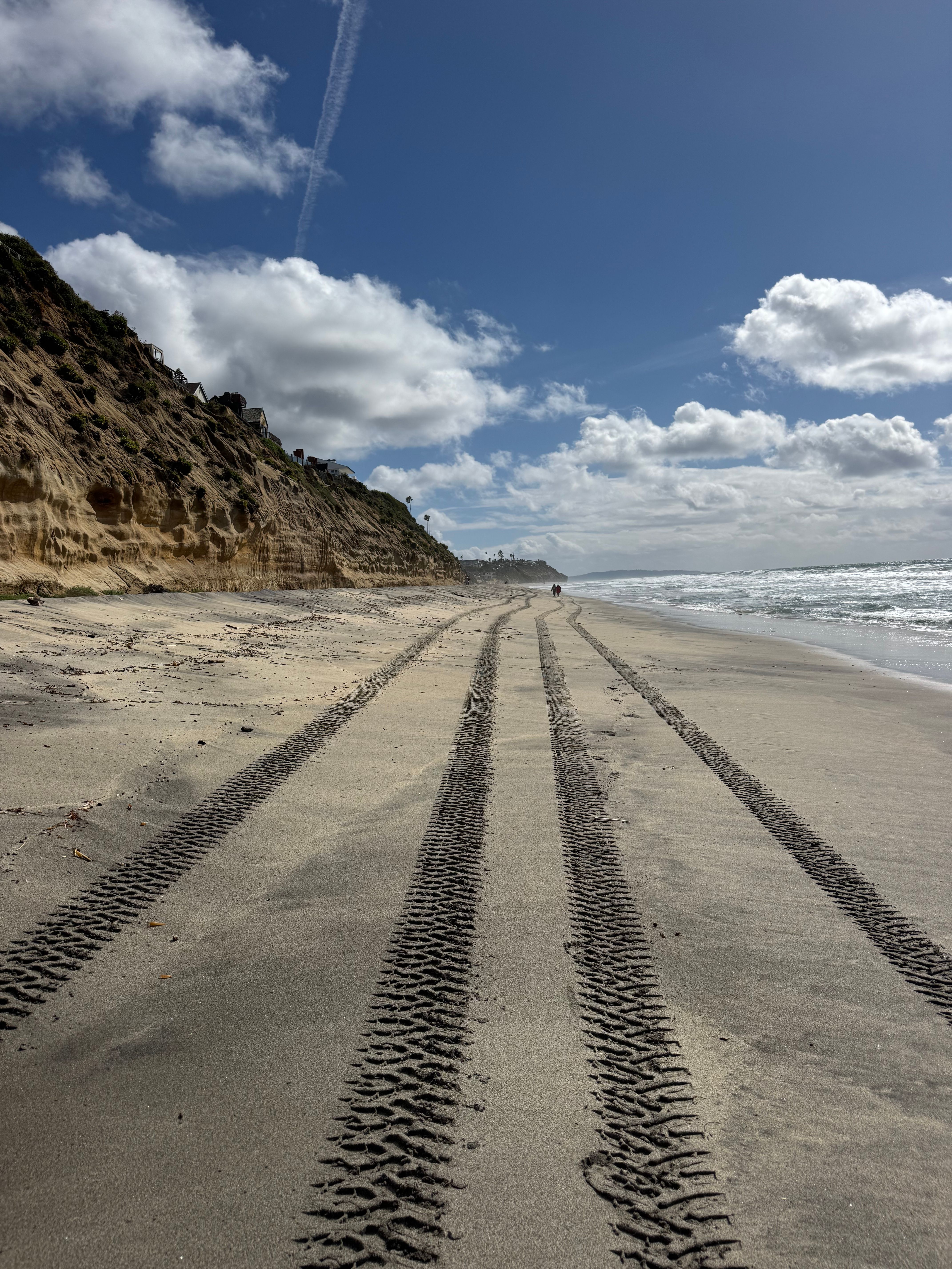 Scenic view of tire tracks on a sandy beach in Encinitas, CA with cliffs and ocean waves.