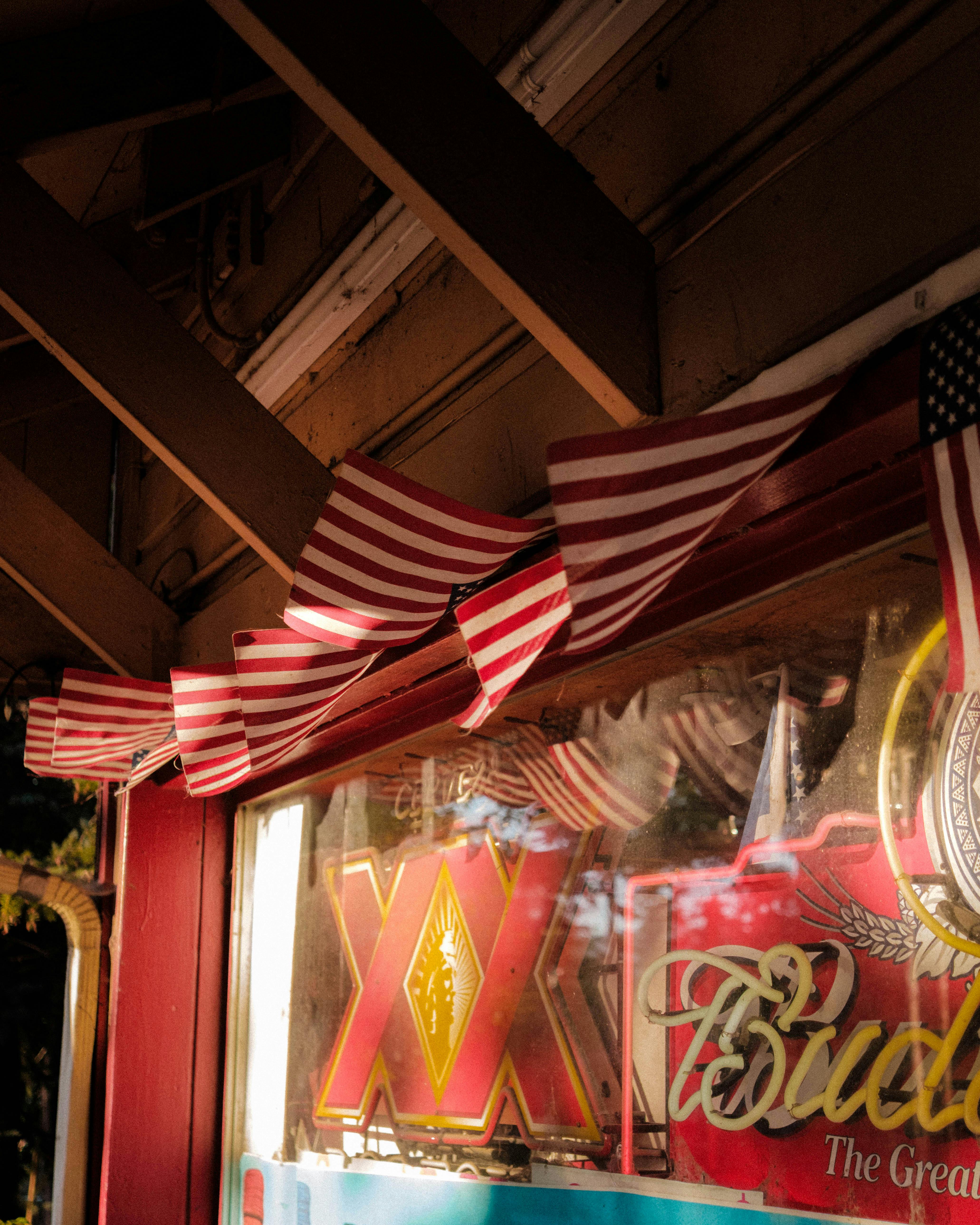 Gratis Pemandangan eksterior sebuah bar yang dihiasi bendera Amerika dan papan nama bir neon. Foto Stok