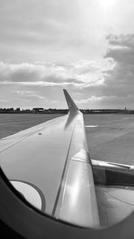 A monochrome view from an airplane window showing the wing and cloudy sky.