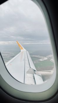 View from an airplane window, showcasing a cloudy sky and coastal landscape below.