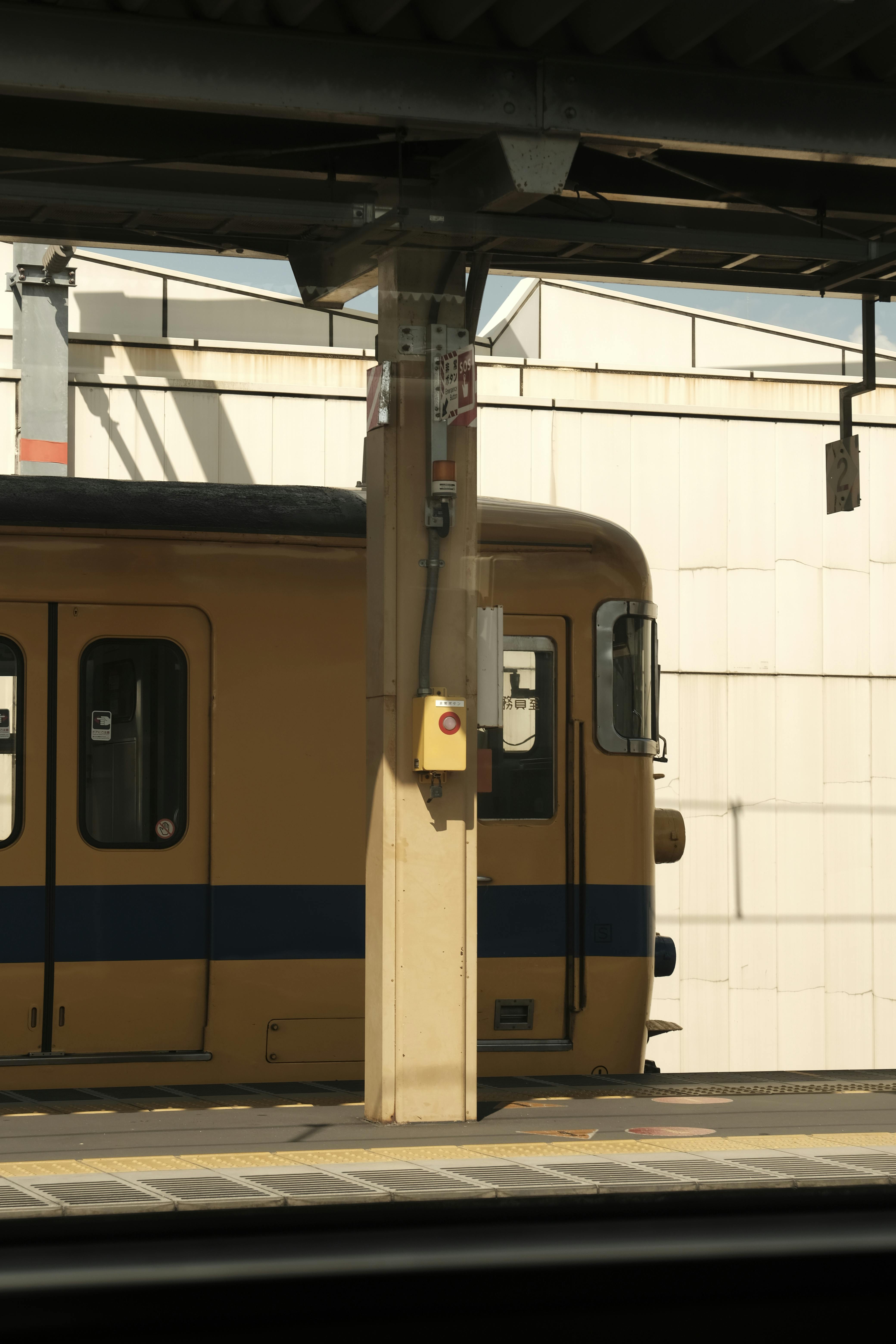 Free A vintage yellow train parked at an empty urban station, emphasizing architectural lines and shadows. Stock Photo