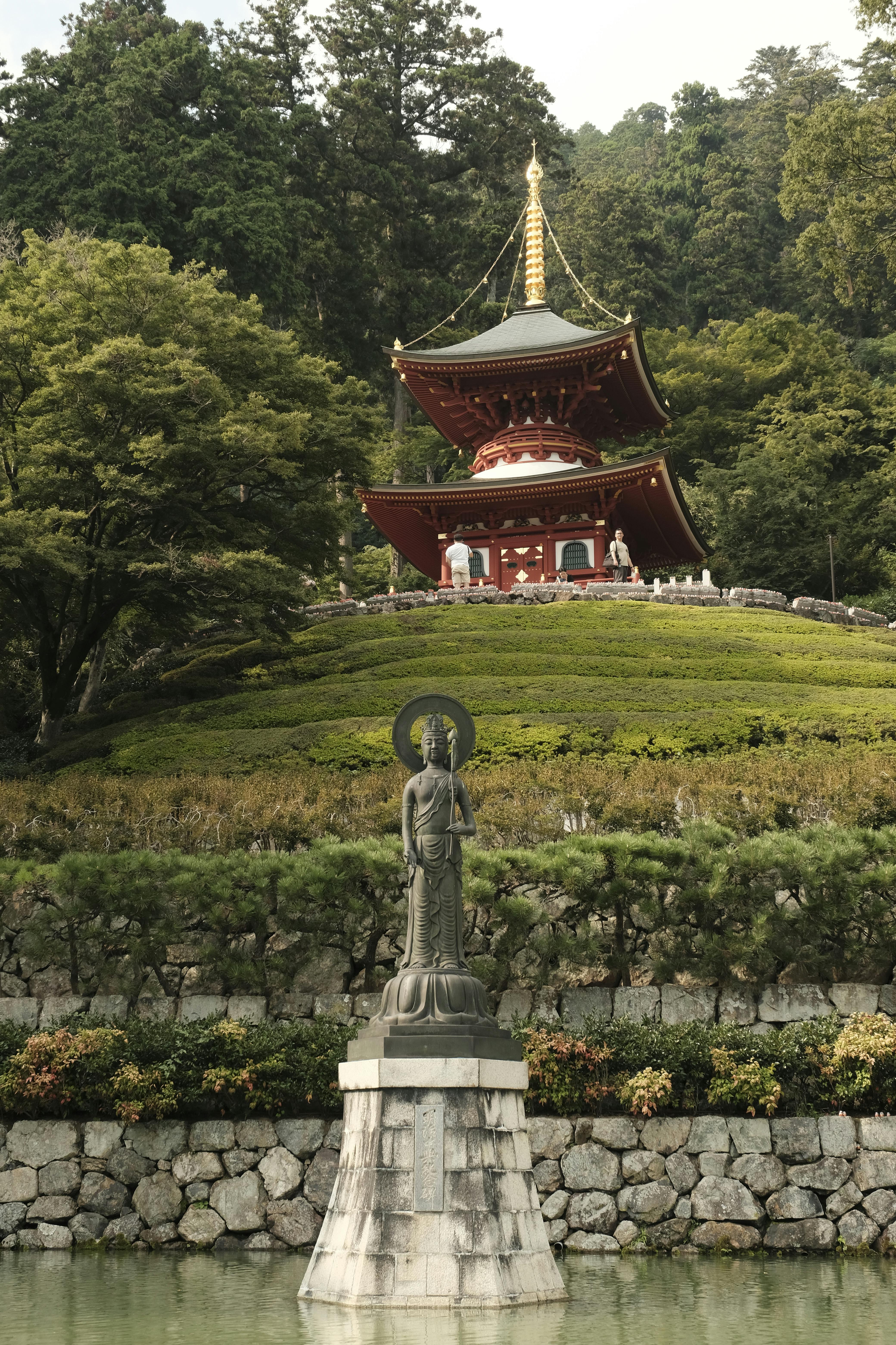 Gratis Taman Jepang yang damai dengan pagoda dan patung, dikelilingi oleh tanaman hijau yang rimbun. Foto Stok