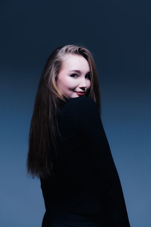 Free Stylish portrait of a young woman with long hair in a black outfit against a blue background. Stock Photo