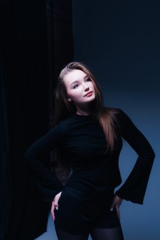 Young woman in black outfit posing confidently in dark studio setting.