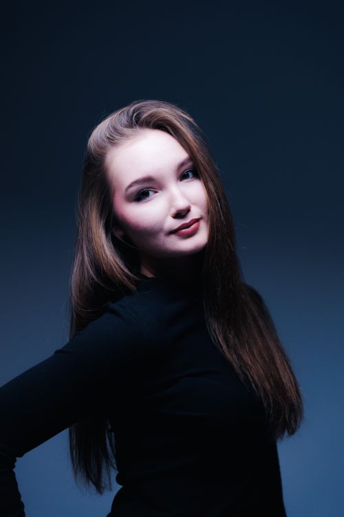 Free Portrait of a young woman in a dark studio setting with a blue tone. Stock Photo
