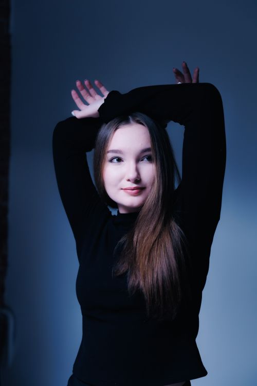 Free A woman poses with her arms raised against a soft blue background in a studio setting. Stock Photo