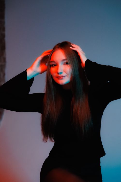 Free A creative portrait of a woman posing with vibrant red and blue lighting in a studio setting. Stock Photo
