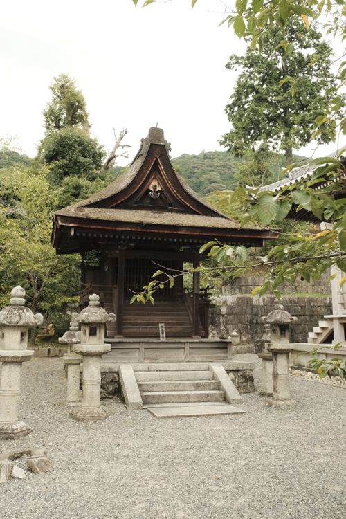Free A serene view of a traditional Japanese temple nestled among lush greenery and stone lanterns. Stock Photo