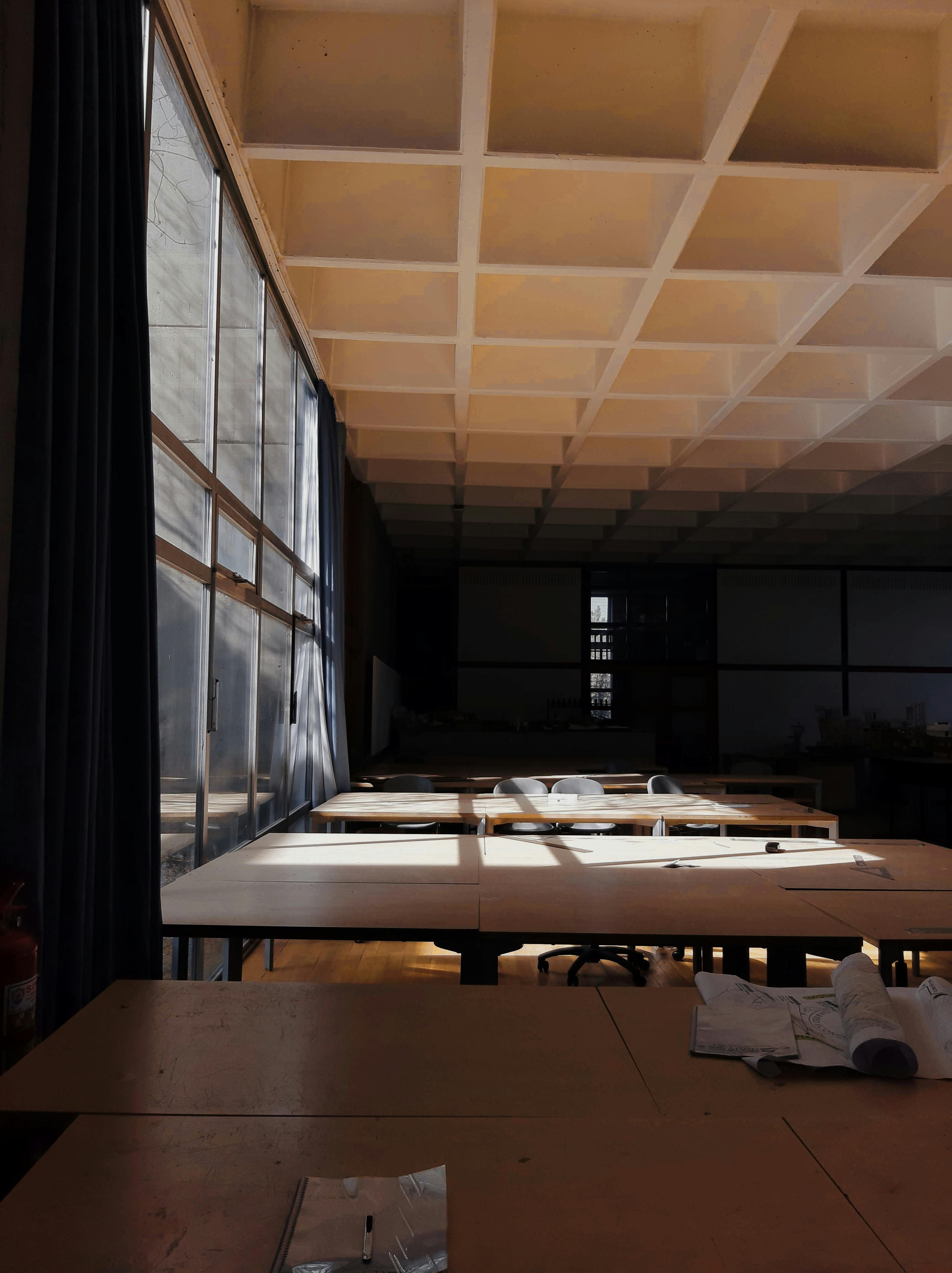 Kostenlos Leeres Klassenzimmer, durch dessen Fenster Sonnenlicht auf die Tische fällt. Stock-Foto