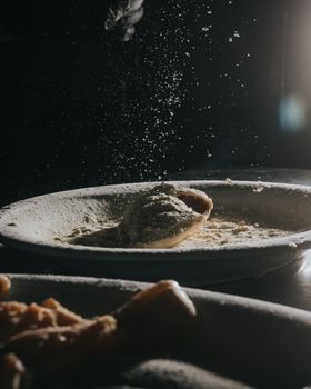 A moody close-up of flour dust settling over a pastry in dim lighting.