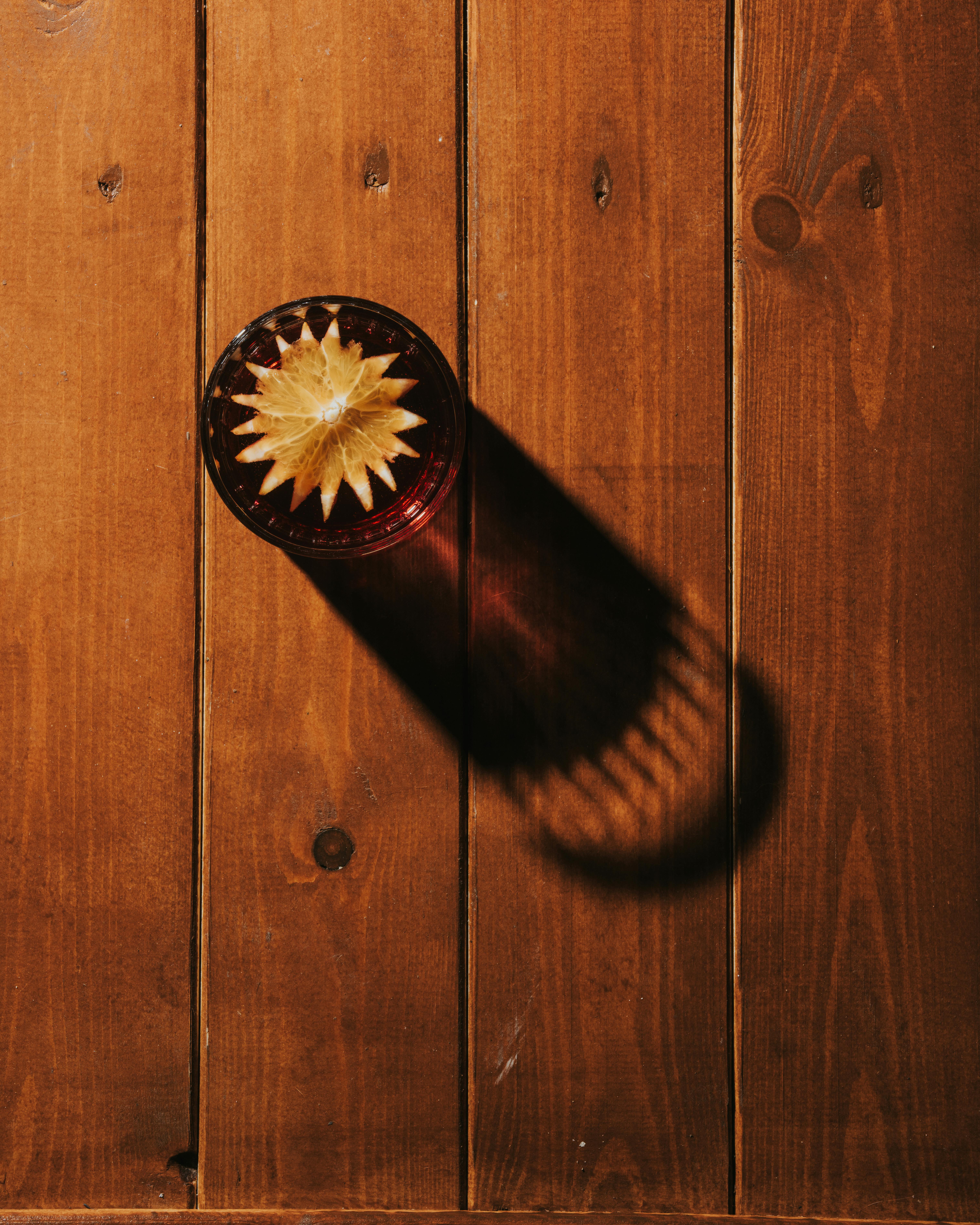 Free A top-down view of a glass on a wooden table casting a long shadow, showcasing artistic lighting. Stock Photo