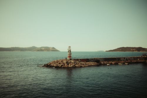 Free Tranquil scene of a lighthouse on a rocky pier overlooking the sea at dawn. Stock Photo