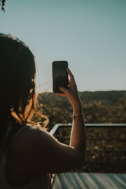 A woman capturing the scenic beauty of sunset using her smartphone, creating a stunning silhouette.