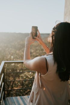 A woman takes a photo of a beautiful outdoor landscape using her smartphone, enjoying the sunny day.