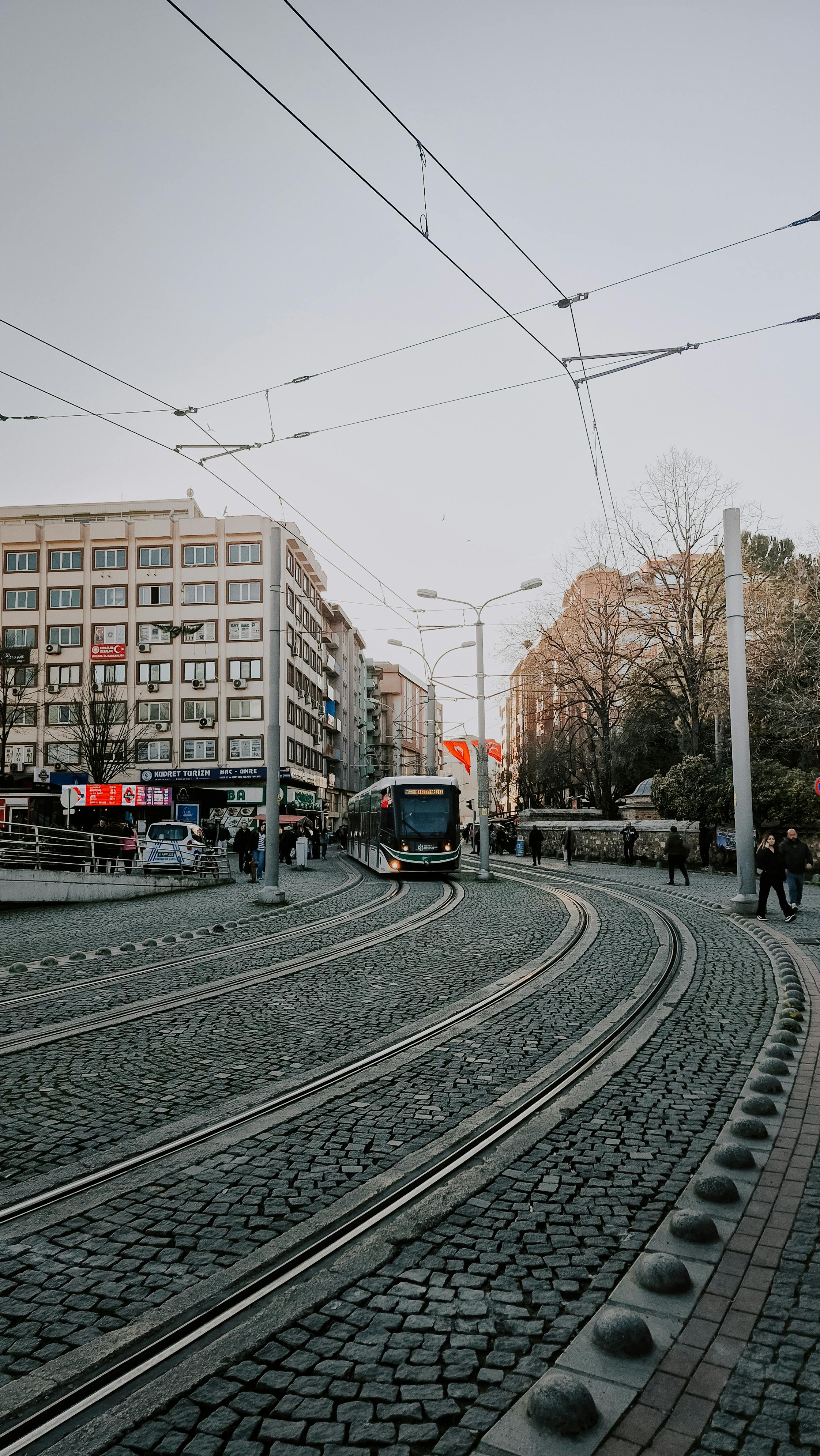 Δωρεάν Αστικό τραμ που κινείται σε έναν καμπυλωτό λιθόστρωτο δρόμο με θέα την αστική αρχιτεκτονική και τους πεζούς. Φωτογραφία από στοκ φωτογραφιών