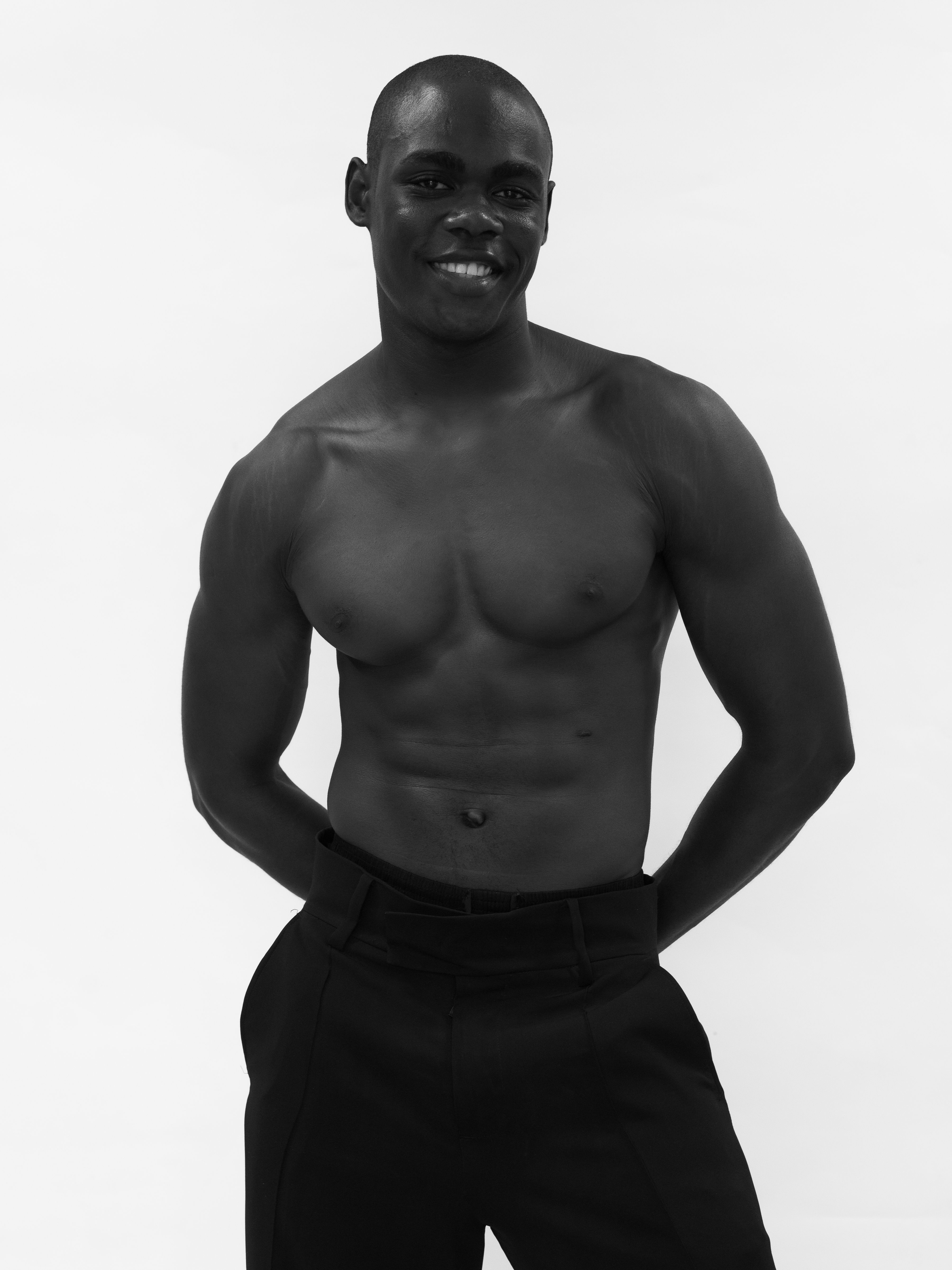 Black and white portrait of an athletic male model with a confident smile, showcasing his physique.