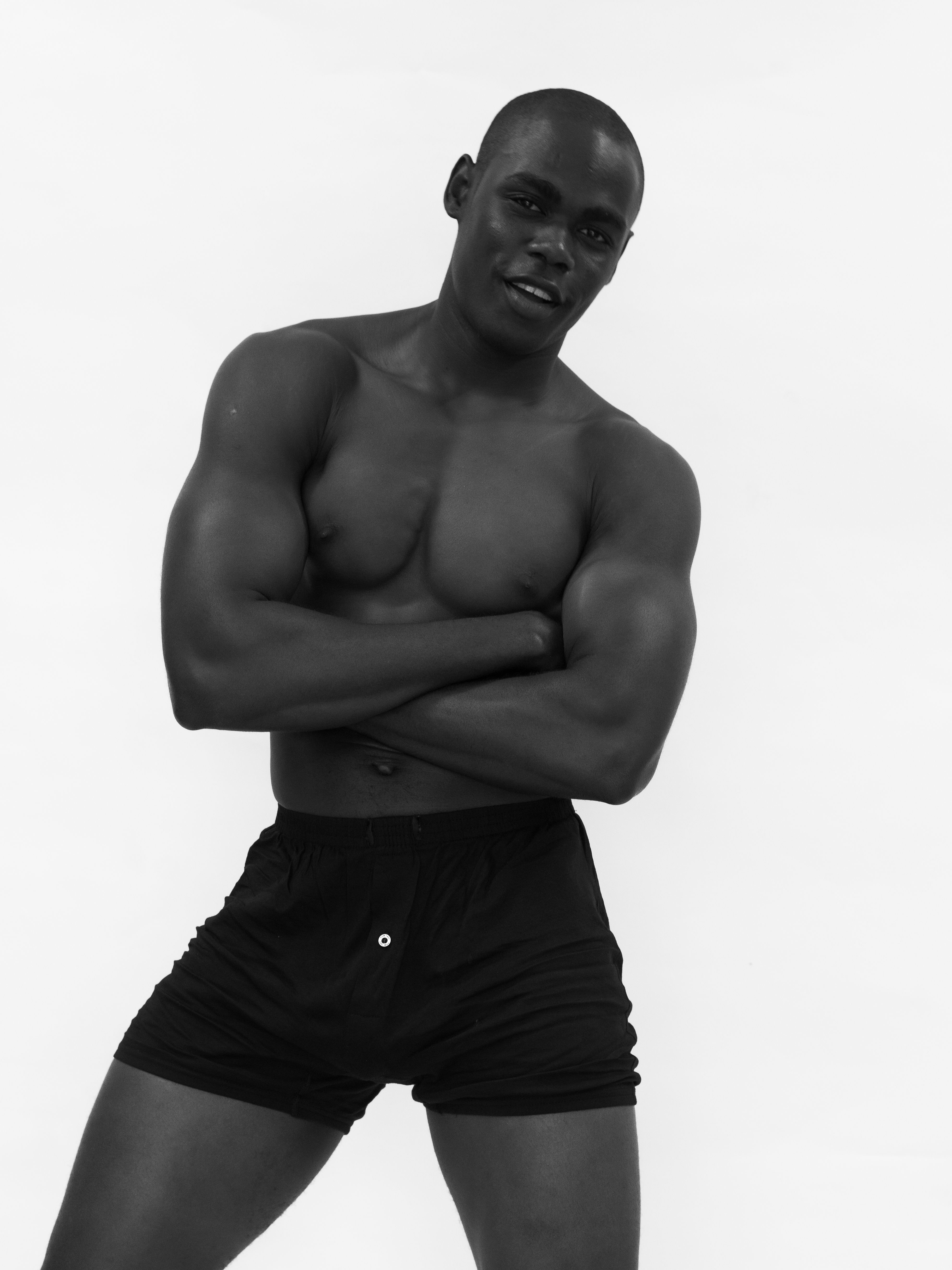 Black and white portrait of a muscular male model in shorts, arms crossed.