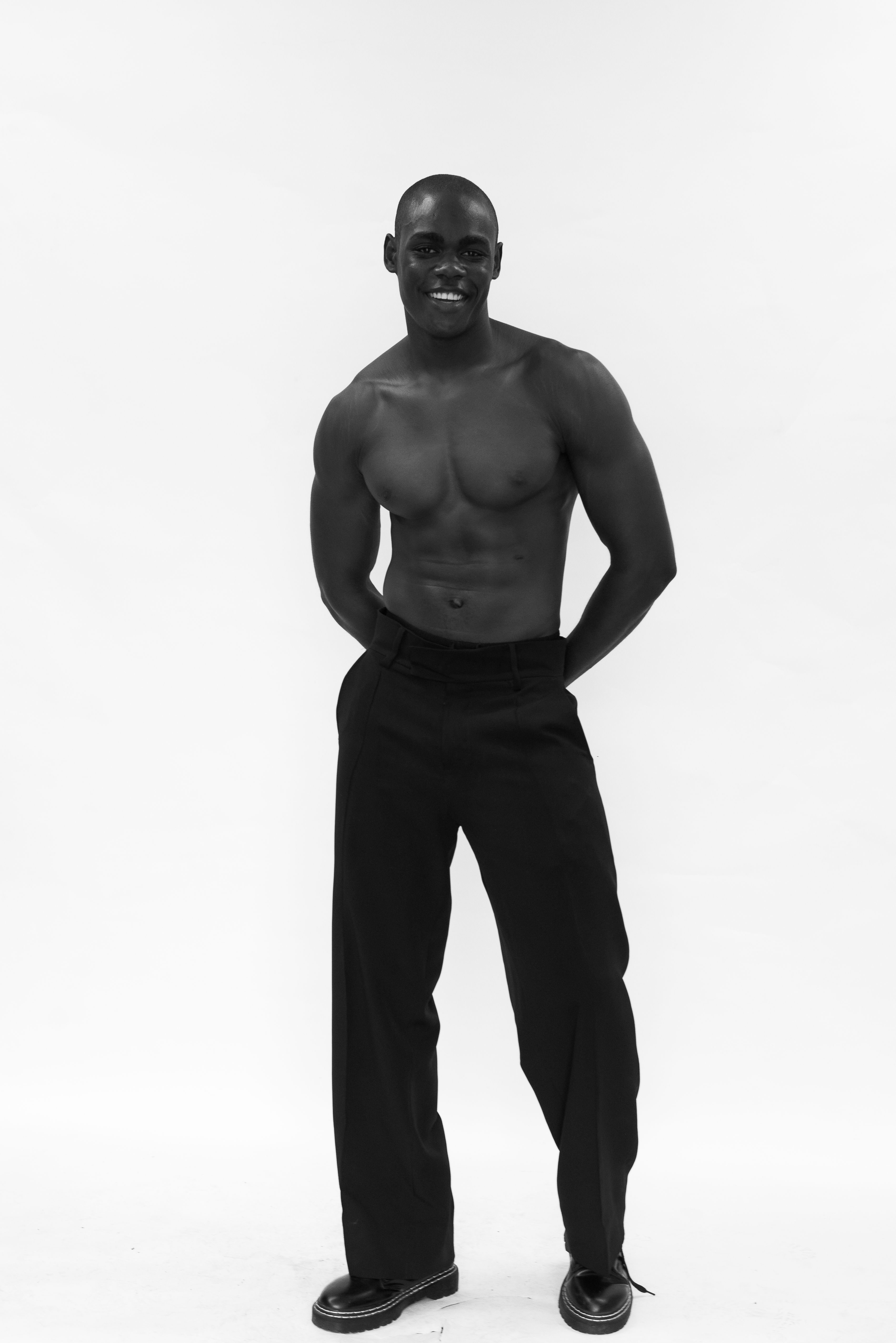 Black and white portrait of a smiling man posing confidently in stylish trousers.