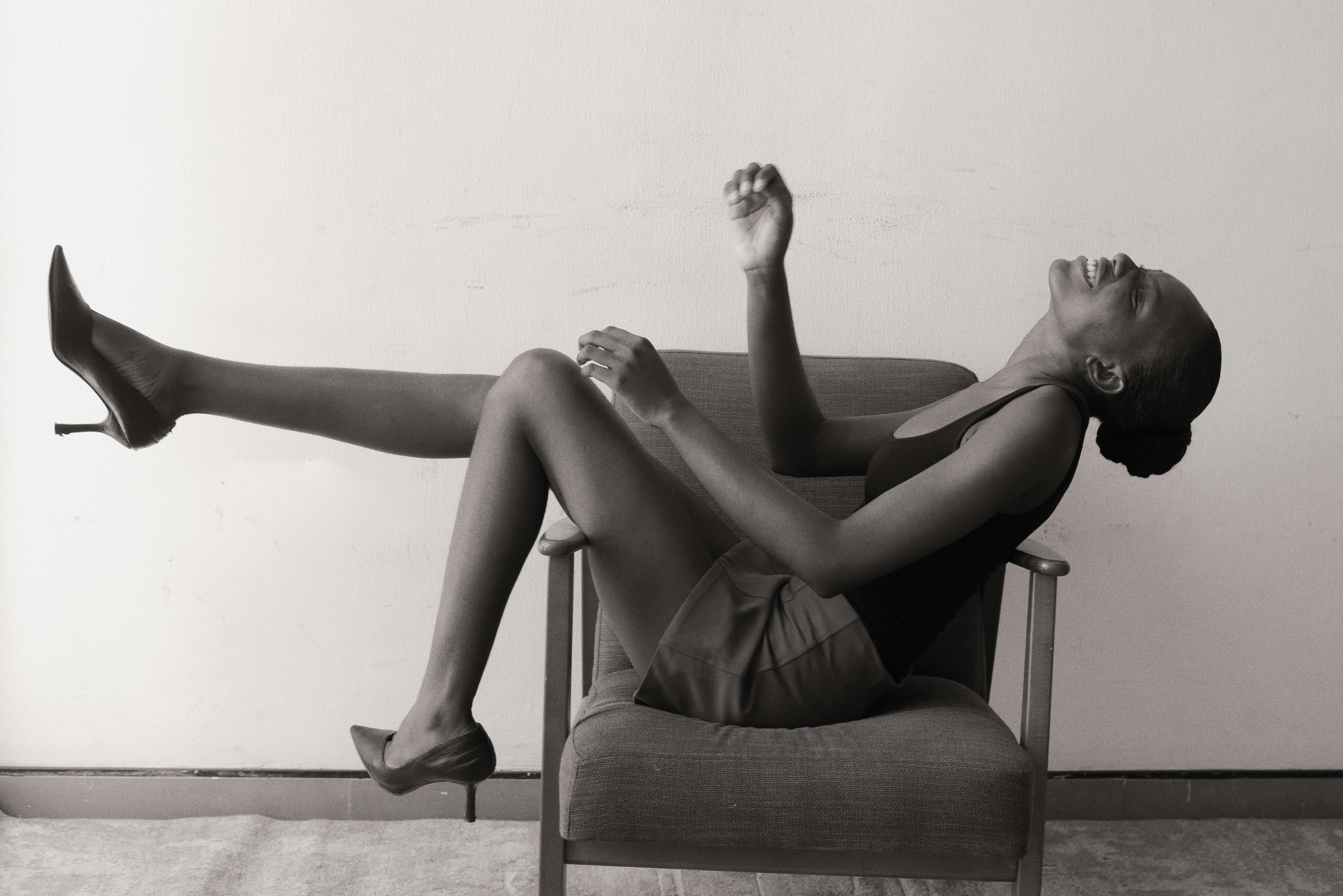 Δωρεάν Ασπρόμαυρη εικόνα μιας χαμογελαστής γυναίκας που ποζάρει κομψά σε μια καρέκλα σε εσωτερικό χώρο στο Λάγος της Νιγηρίας. Φωτογραφία από στοκ φωτογραφιών