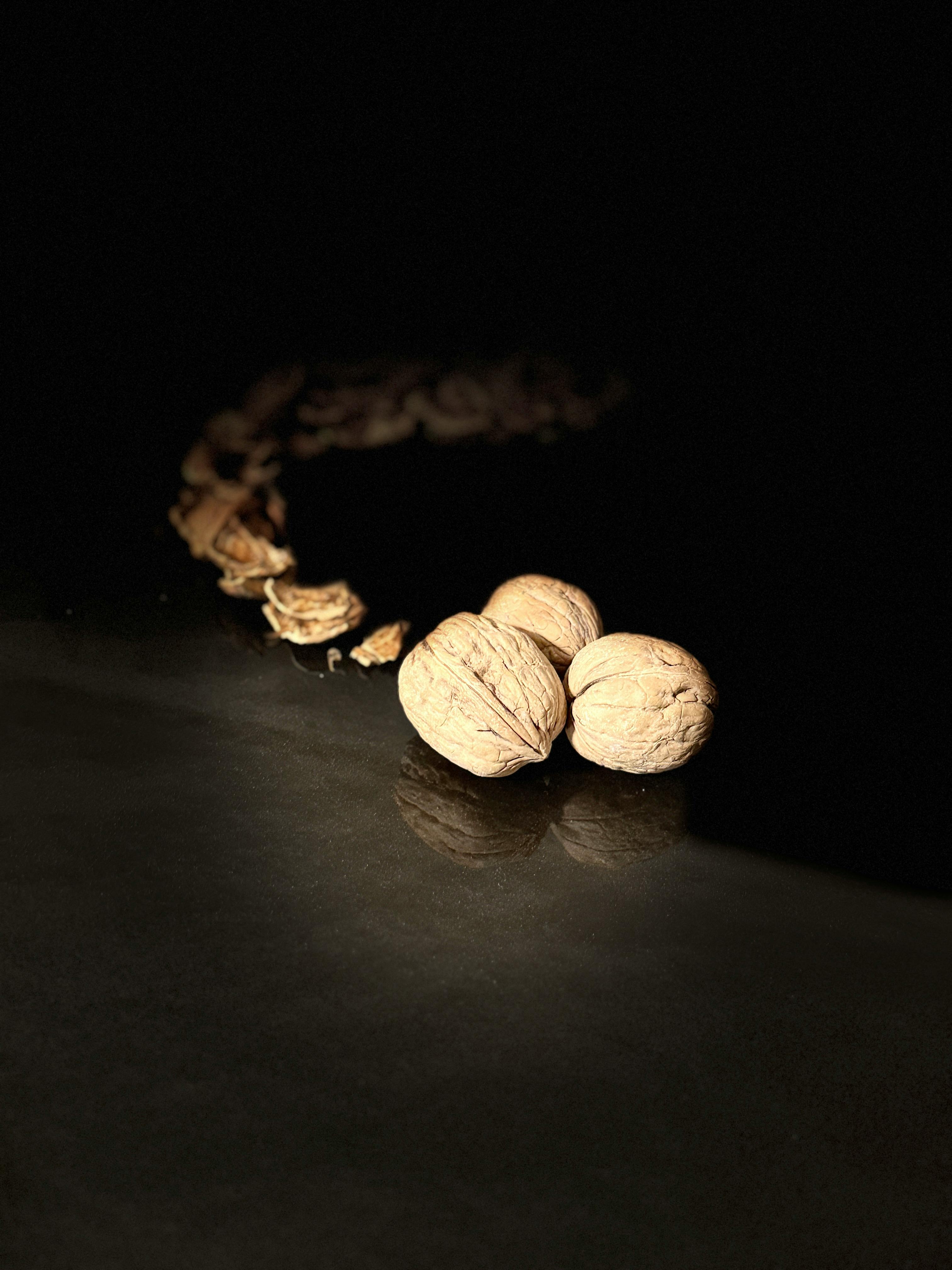 Kostenlos Künstlerische Fotografie von Walnüssen auf dunklem Untergrund mit dramatischer Beleuchtung, die eine stimmungsvolle Stilllebenszene erzeugt. Stock-Foto