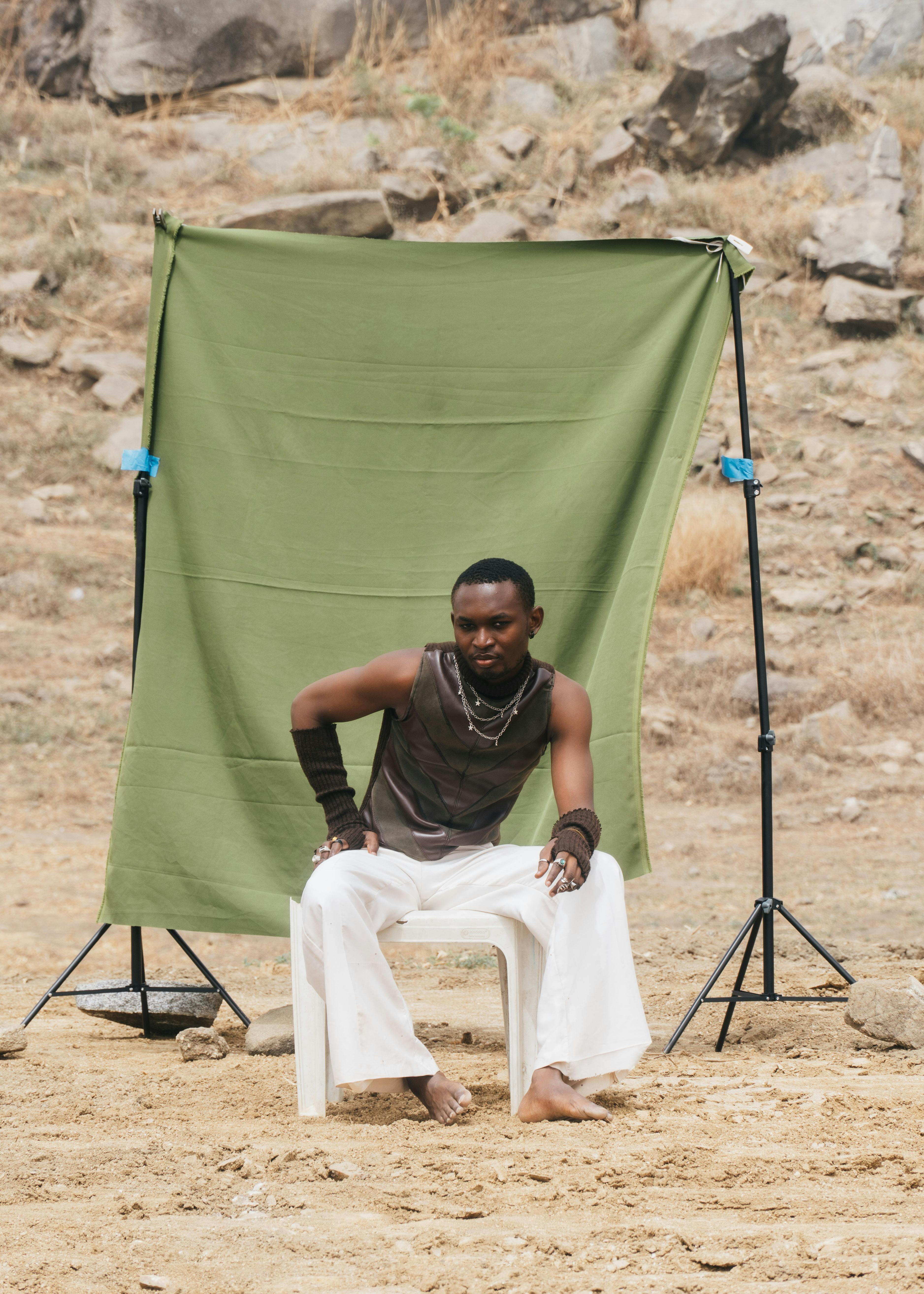 Man sitting on a chair outdoors with a green fabric background in Abuja, Nigeria.